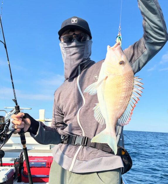 鳥取での根魚ジギングの釣果。青空の下、お客様が綺麗な魚を高々と掲げて記念撮影。