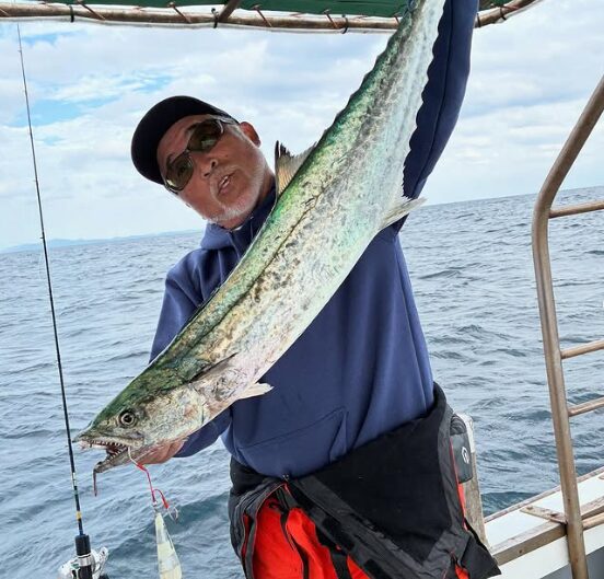 鳥取の遊漁船でのジギング釣果。青いパーカーにサングラス姿の釣り人が、メタルジグで釣り上げた大きなサワラを誇らしげに掲げている。