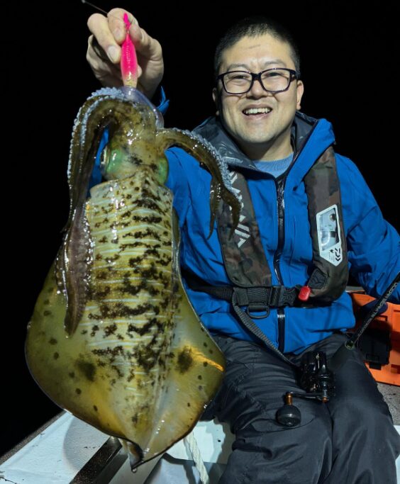ティップランで釣り上げたばかりのアオリイカと、その釣果に満足げな釣り人の笑顔。夜の船上で撮影