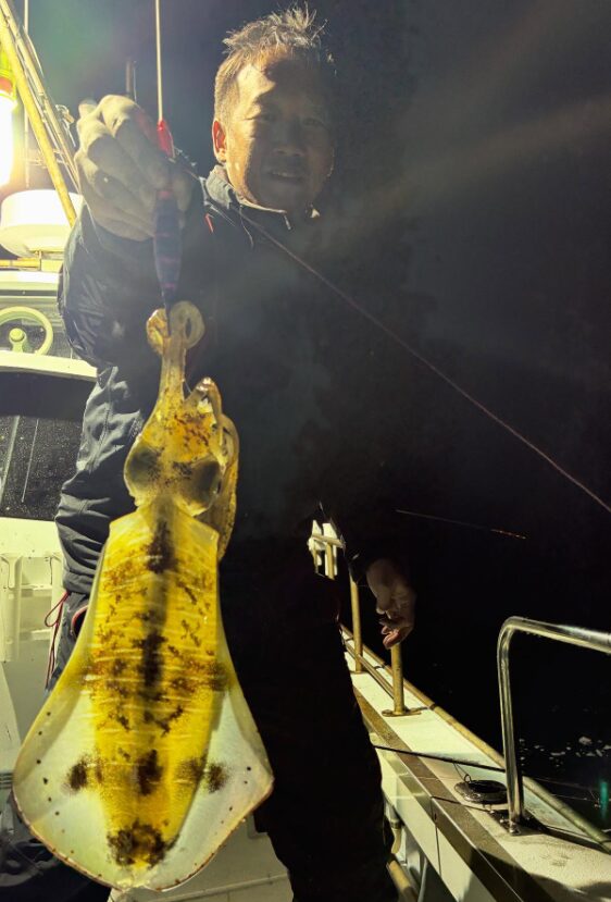 鳥取沖でのティップラン釣果！夜の船上で、釣り上げたばかりのアオリイカを誇らしげに見せる釣り人