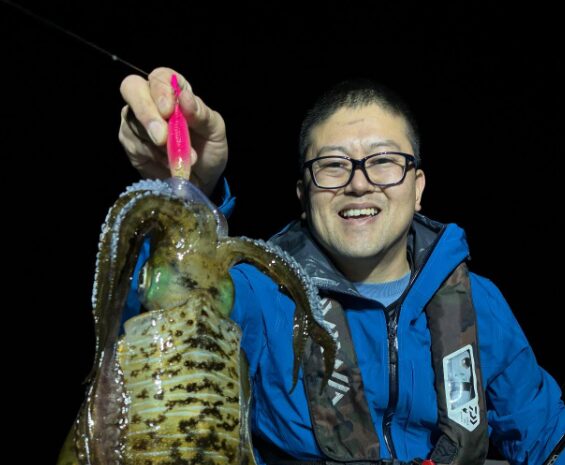 ティップランで釣り上げたばかりのアオリイカと、その釣果に満足げな釣り人の笑顔。夜の船上で撮影