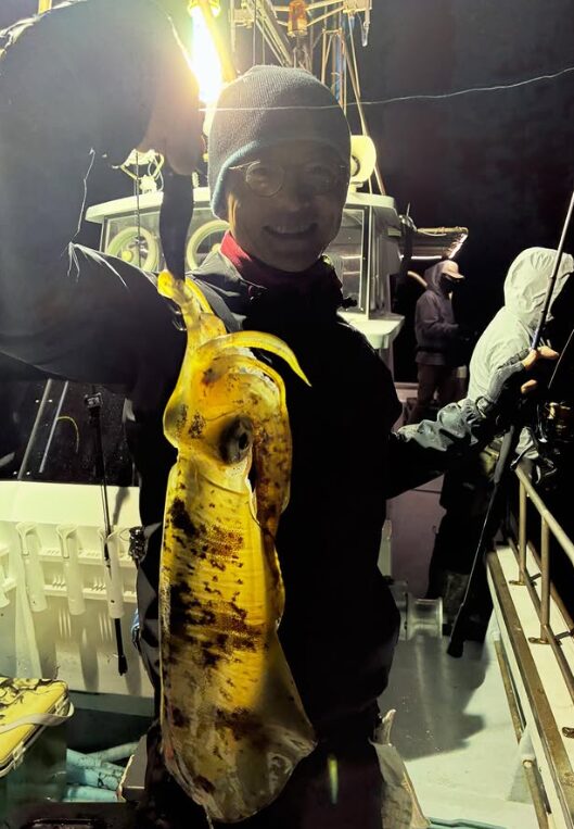 鳥取のアオリイカティップランにて、グレーのニット帽と眼鏡をかけたお客様が笑顔で良型を掲げている様子