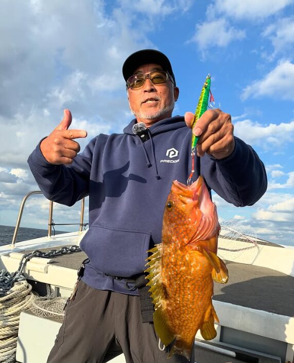 鳥取の釣り船でジギングを楽しむ重見プロ。プレッジのジグで釣り上げた見事なアコウ（キジハタ）を手に、笑顔でポーズをとる様子。