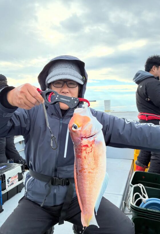 鳥取での根魚ジギングにて貴重なゲスト。グレーのハットと眼鏡をかけた男性が、フィッシュグリップを使用して高級魚のアマダイを掲げている一枚。